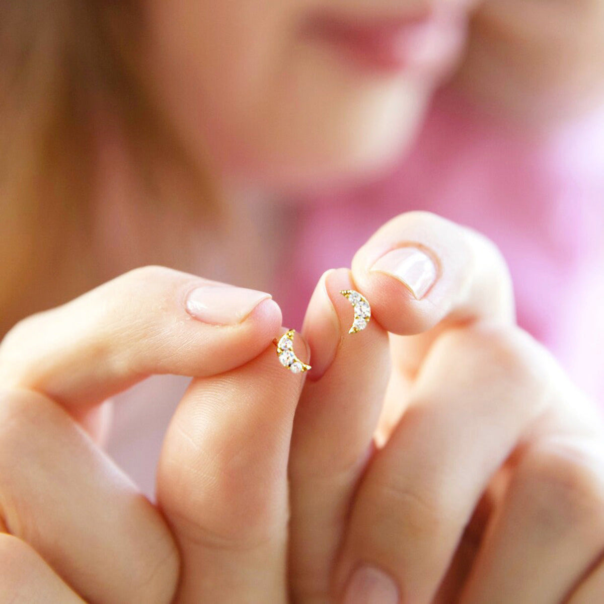 A person's hand holding a small gold-coloured earring stud with a crystal moon design.