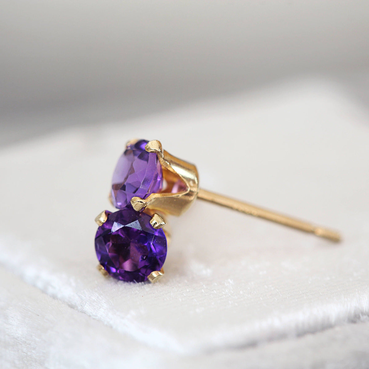 A pair of matching gemstone stud earrings in gold settings. The amethyst gemstone is round, faceted, sparkling and pale lavender purple in colour. The stones are set into 14k gold fill ear posts with a 4 prong setting with matching butterfly backs.