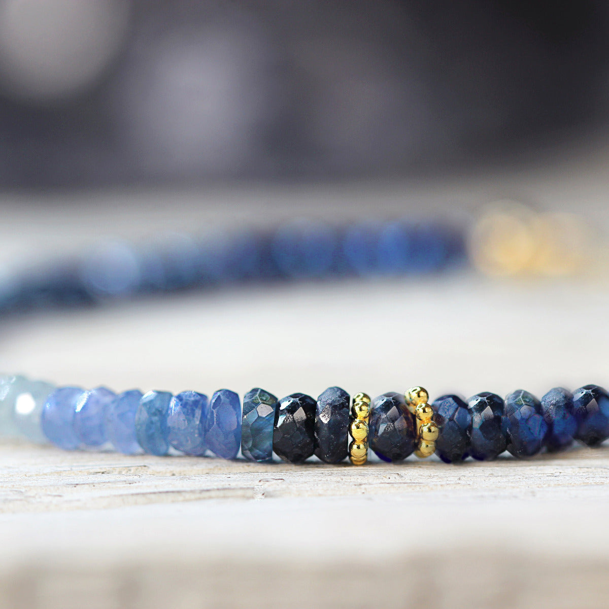 Blue beaded sapphire bracelet with gold accents on a wooden surface