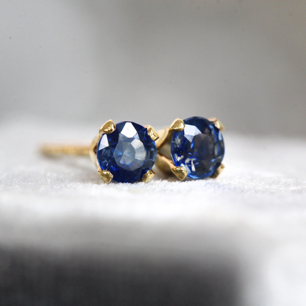 Handmade 14k gold fill stud earrings featuring faceted, sparkling, brilliant round cut deep indigo blue sapphire gemstones set into a 4 prong setting. The earrings are round in shape, with ear post fitting and butterfly backs. Simple and minimal in style.