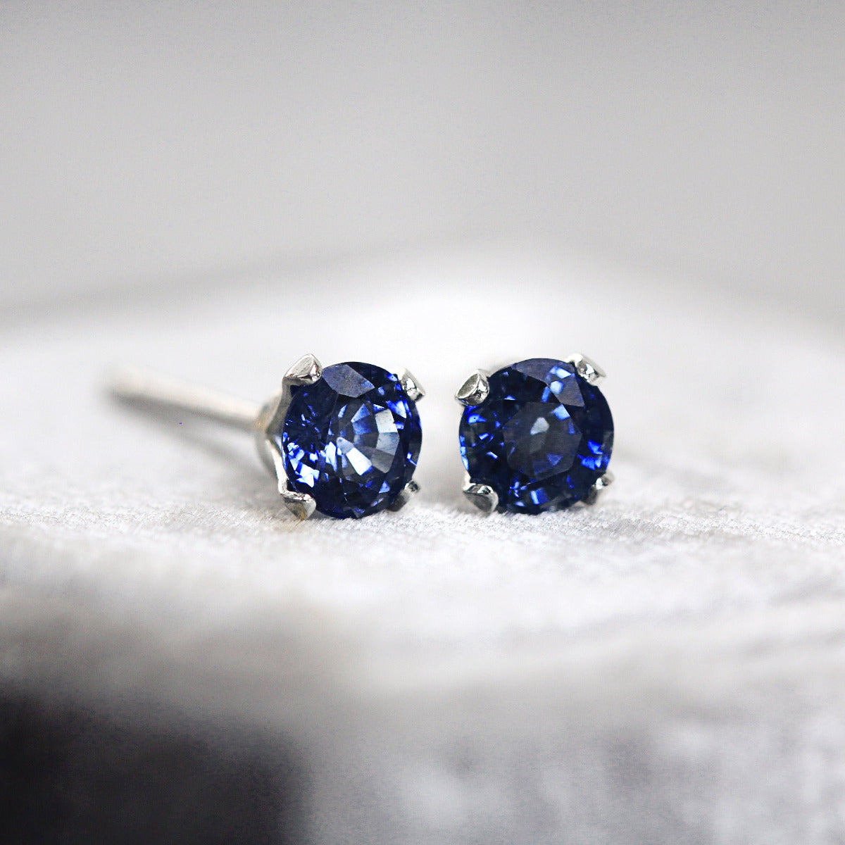 Pair of blue gemstone stud earrings in silver setting on a light gray background