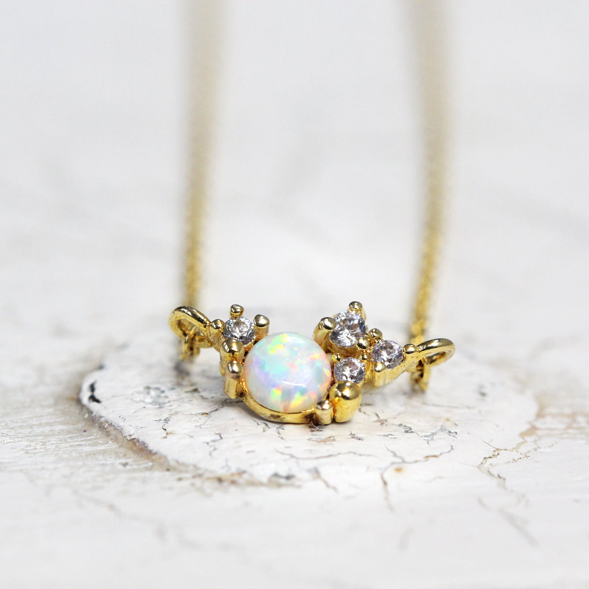 A gold-colored cubic zirconia birthstone cluster necklace with a gold-plated chain, displayed against a white textured background.