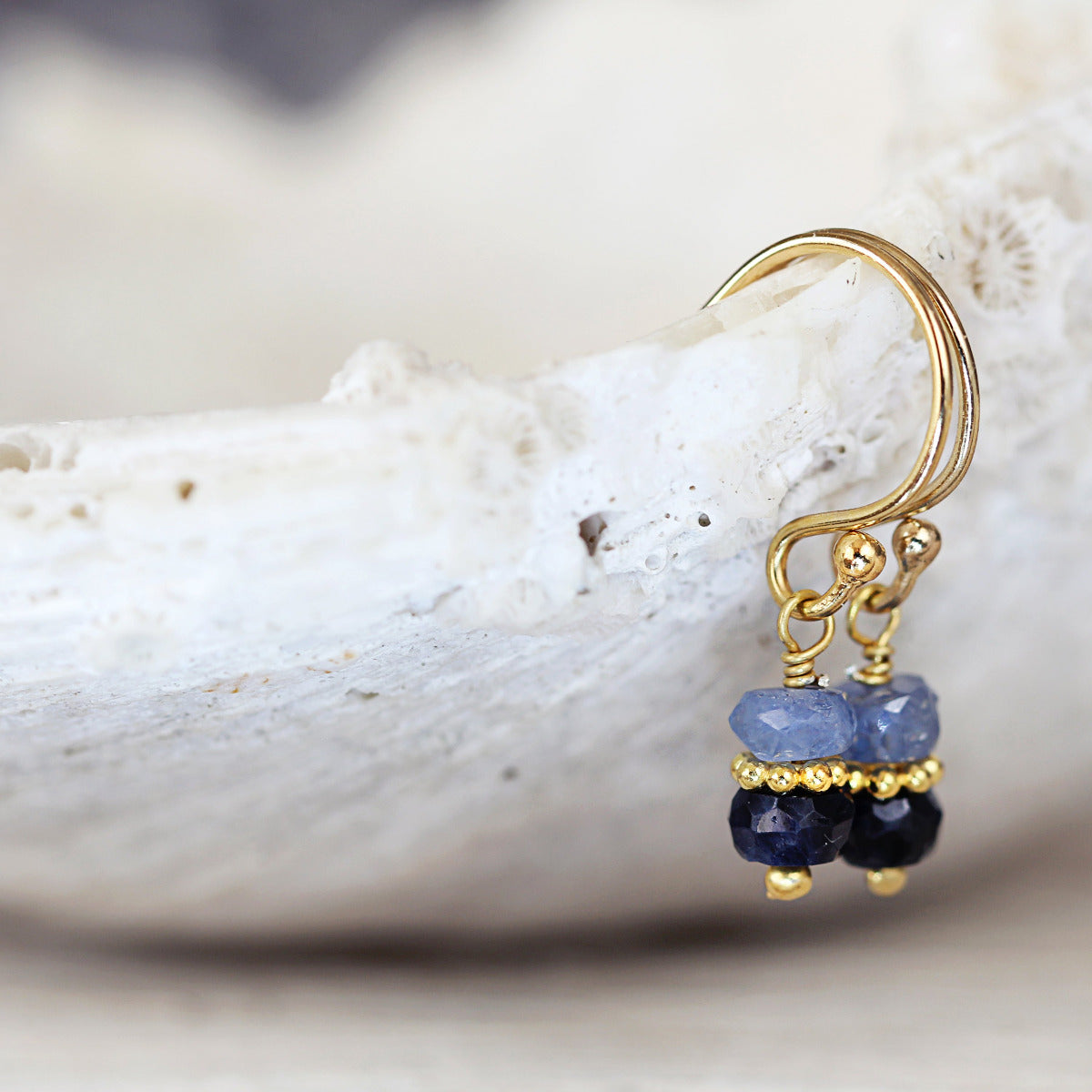 Gold earrings with blue sapphire gemstones on a shell background