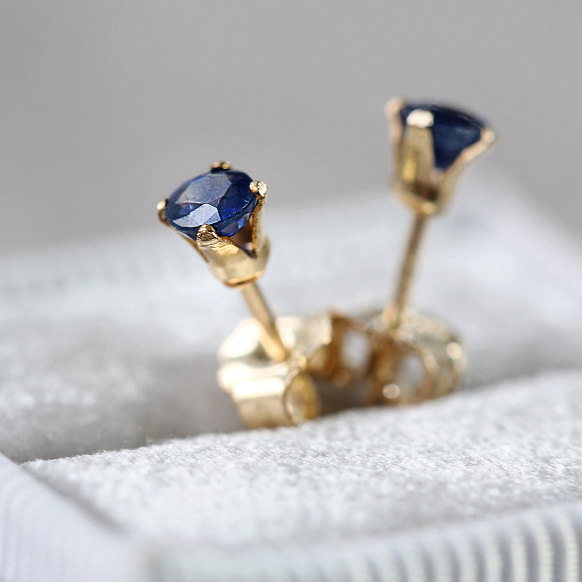 Gold stud earrings with dark blue sapphire gemstones on a textured surface