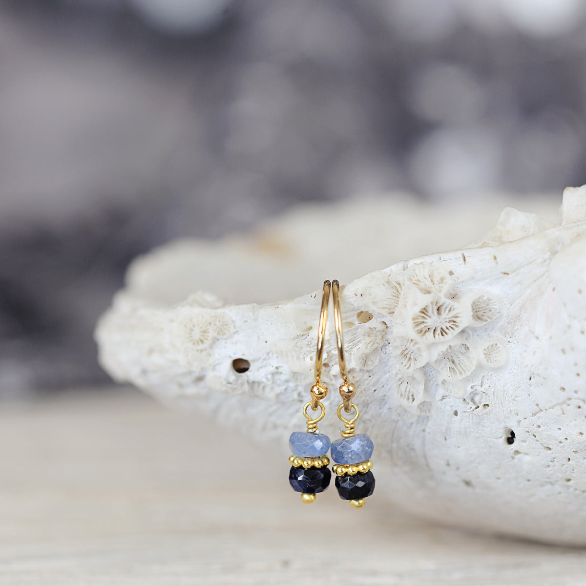Gold earrings with blue sapphire beads on a white stone background