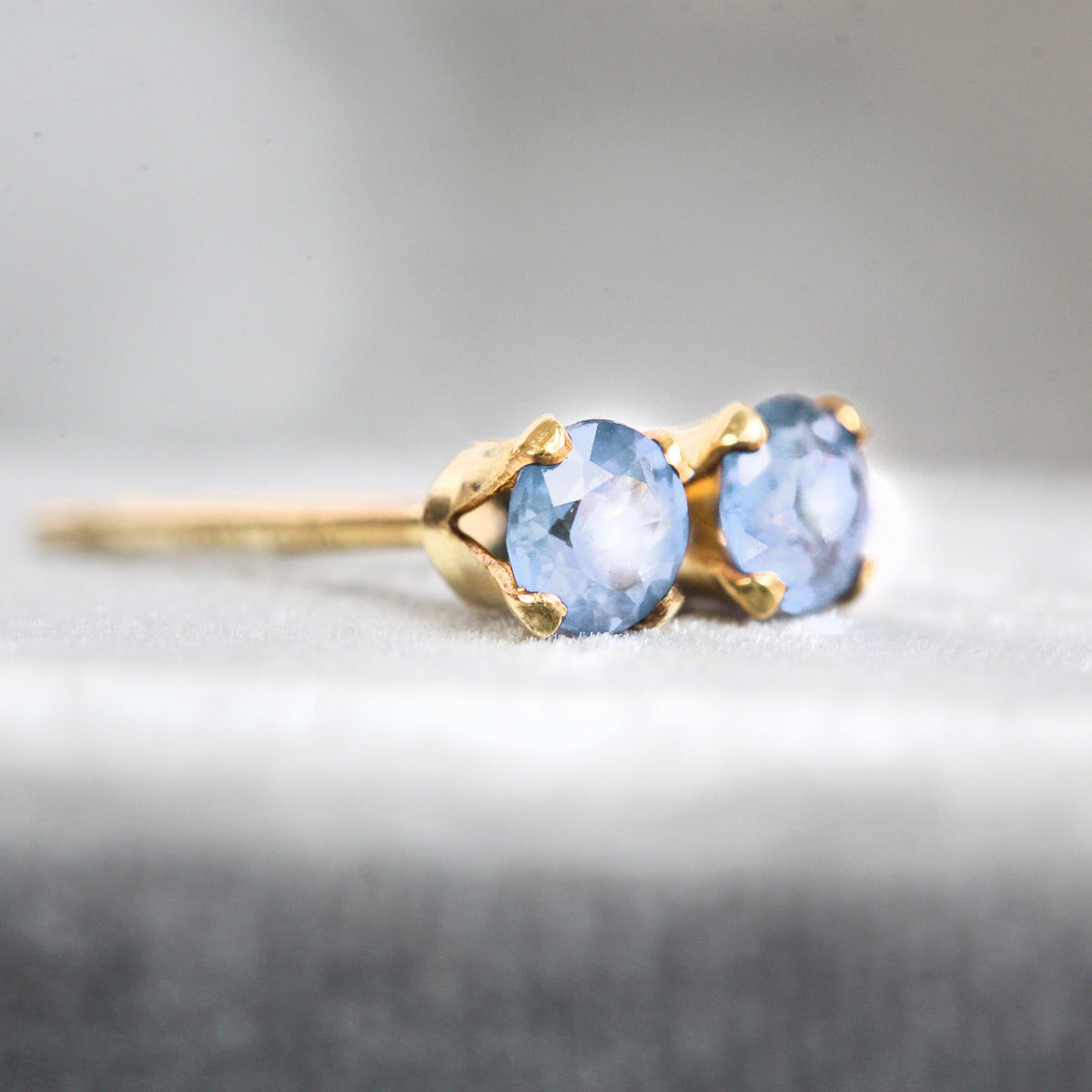 Gold earrings with light blue sapphire gemstones on a gray background