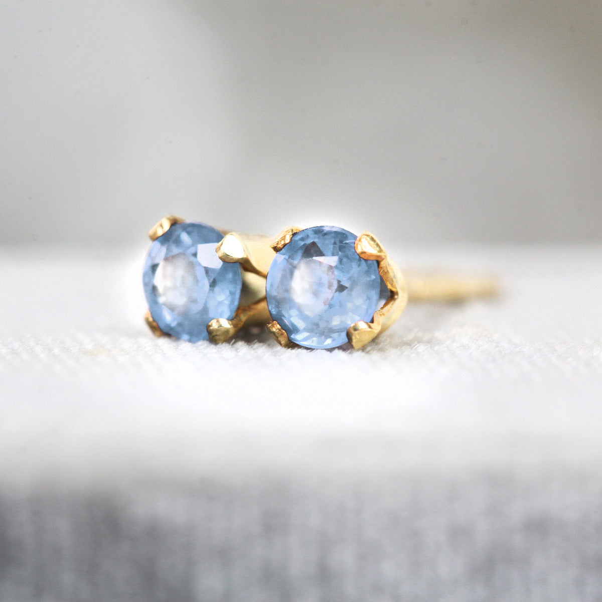 Gold stud earrings with blue sapphire gemstones on a textured surface