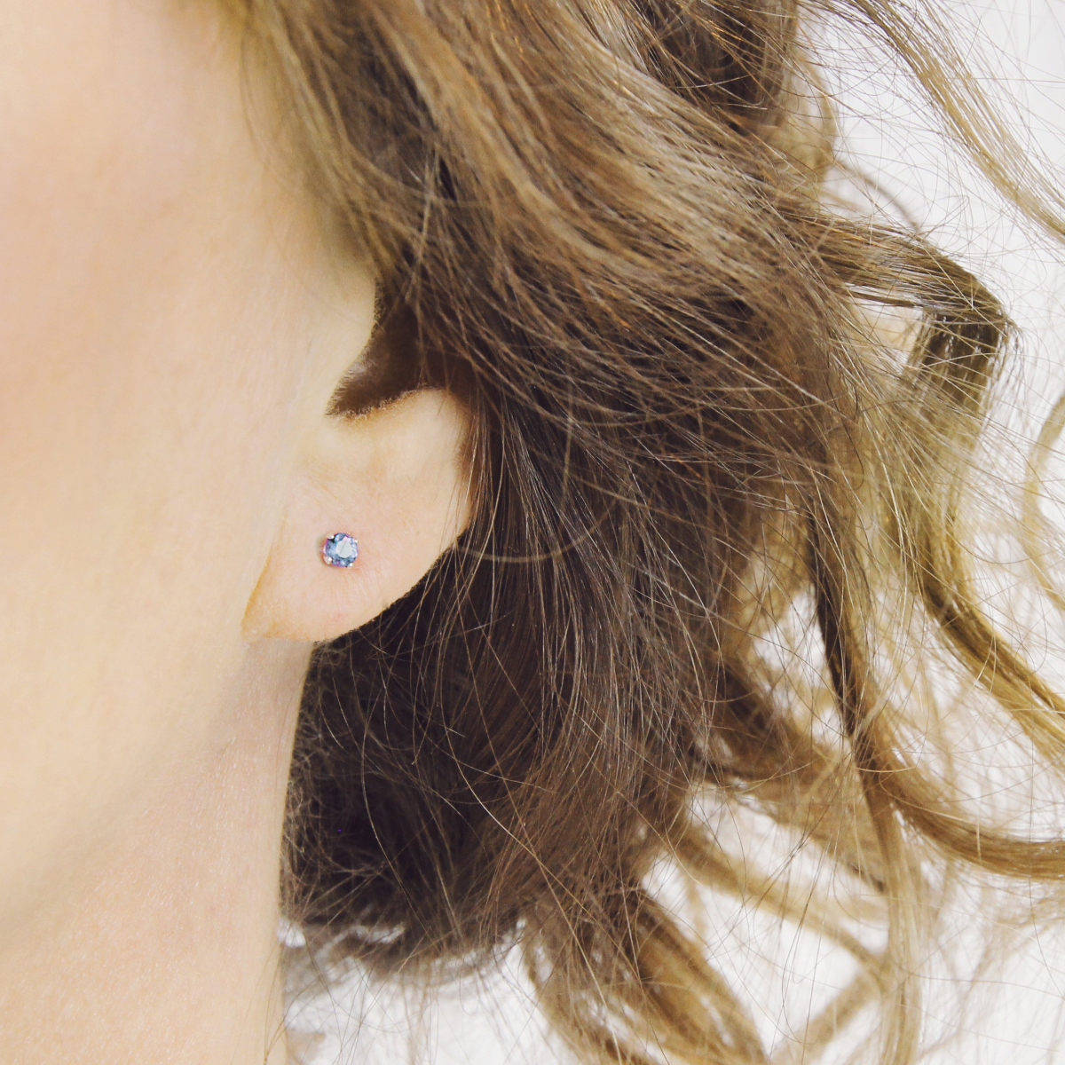 A light blue sapphire stud earrings worn by a person with wavy hair.