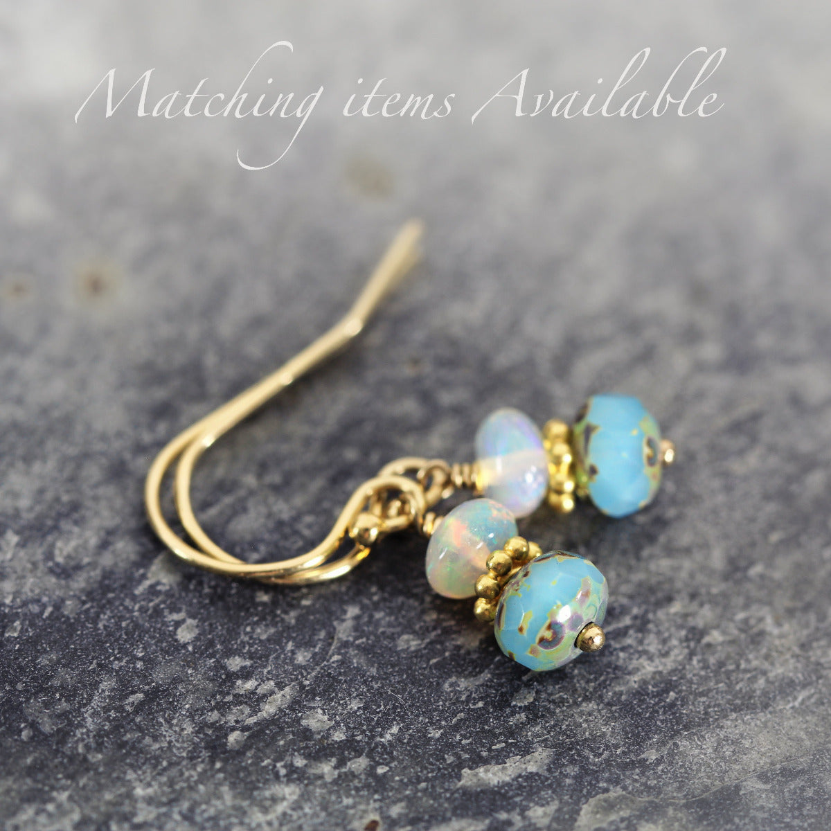 Gold earrings with blue and white opal beads on a gray surface.