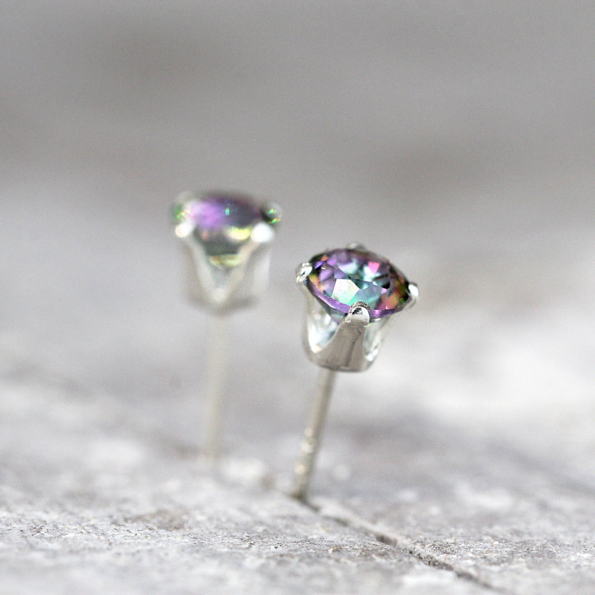 Gemstone stud earrings showcasing mystic topaz stones set into sterling silver ear posts. The topaz gemstones are a brilliant round cut and are colourful, dazzling and sparkling. The ear posts are sterling silver four prong settings with push backs.