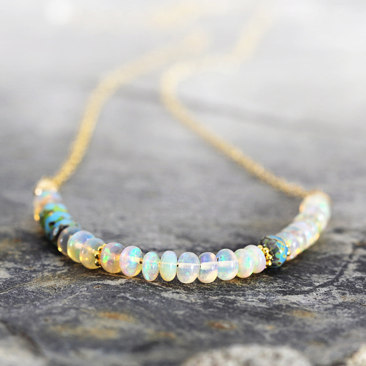 Opal beaded necklace with gold chain on a stone surface