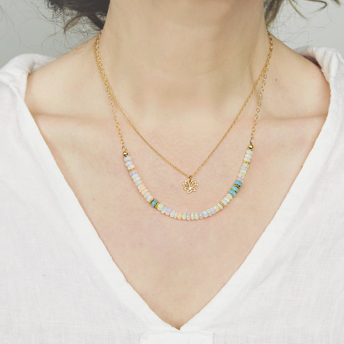 Gold necklace with opal beads and a gold chain on a person wearing s white shirt