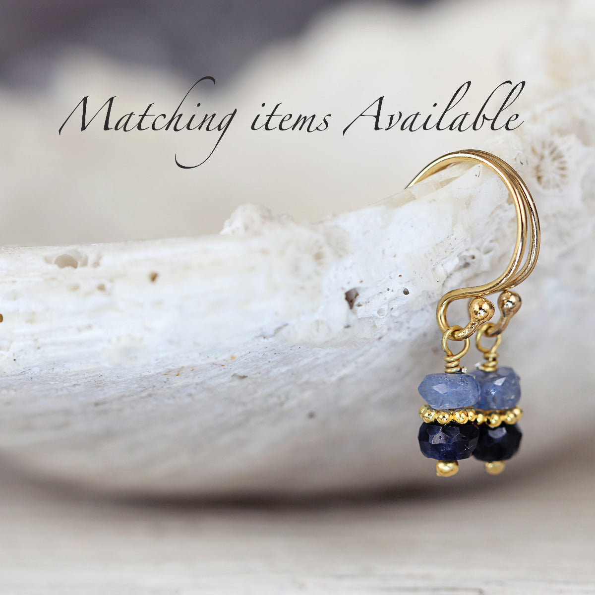 Gold earring with blue sapphire gemstones on a white shell background