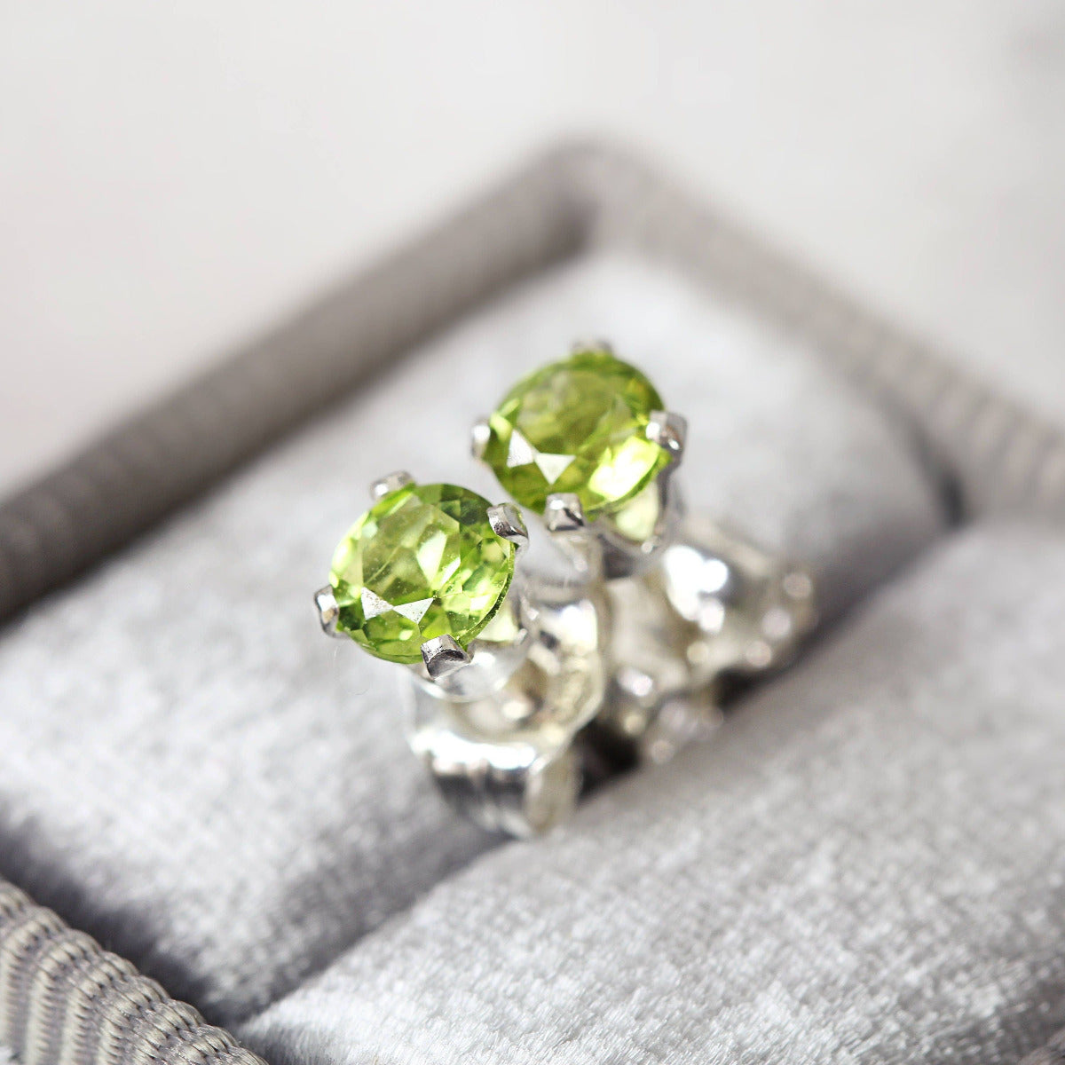 Handmade sterling silver stud earrings featuring faceted, vibrant green peridot gemstones in a prong setting. Round in shape, with ear post fitting and matching butterfly backs. The earrings are simple and minimal in style, and come in various sizes.