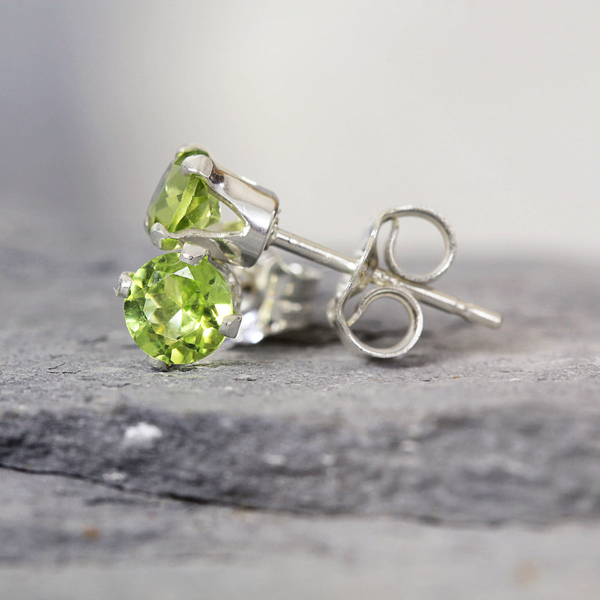 One pair of bright green peridot stud earrings. The peridot stone is round in shape with a facted cut. The 14k gold fill ear post setting has four prongs holding the gemstone in place, and butterfly push backs to hold the stud securely on the ear.