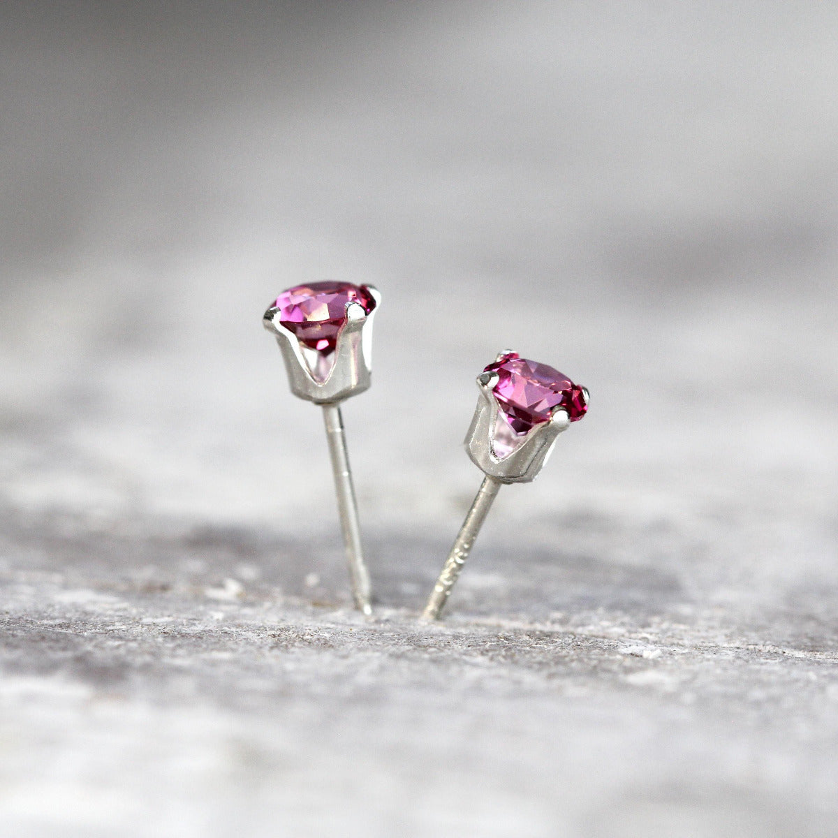 A pair of bright pink topaz stud earrings. The pink topaz gemstones are sparkling and catch the light. The stones are a brilliant round cut with lots of facets, and set into real silver four prong settings. Simple, minimal, round silver stud earrings