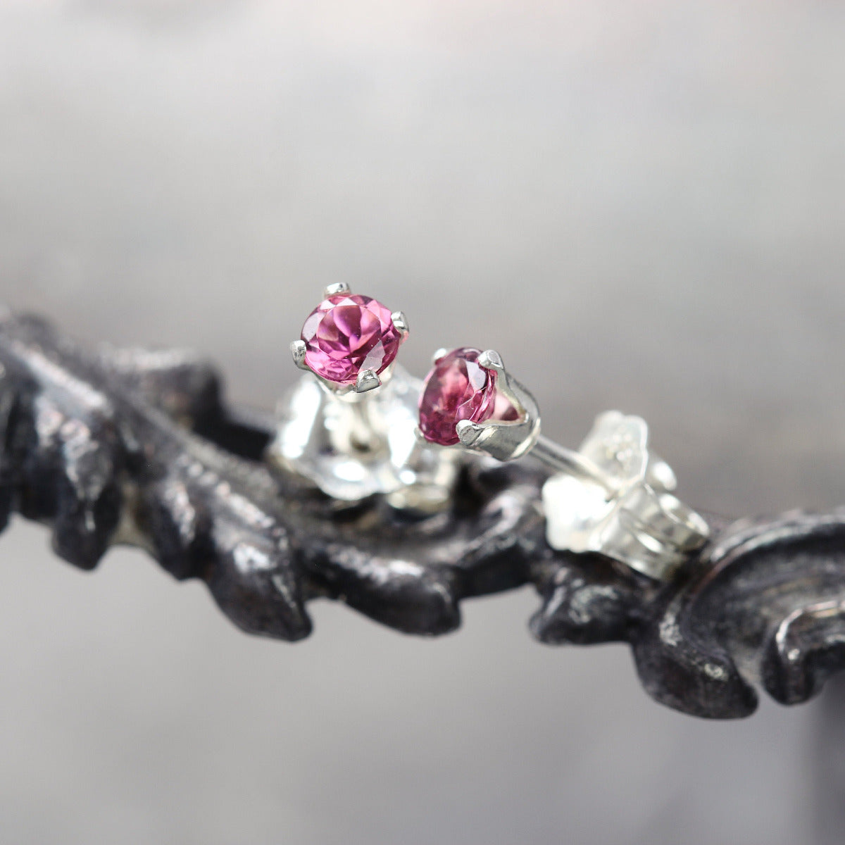 A pair of rose pink tourmaline stud earrings. The tourmaline gemstones are sparkling and catch the light. The stones are a brilliant round cut with lots of facets, and set into sterling silver prong settings. Simple, minimal, round stud earrings.