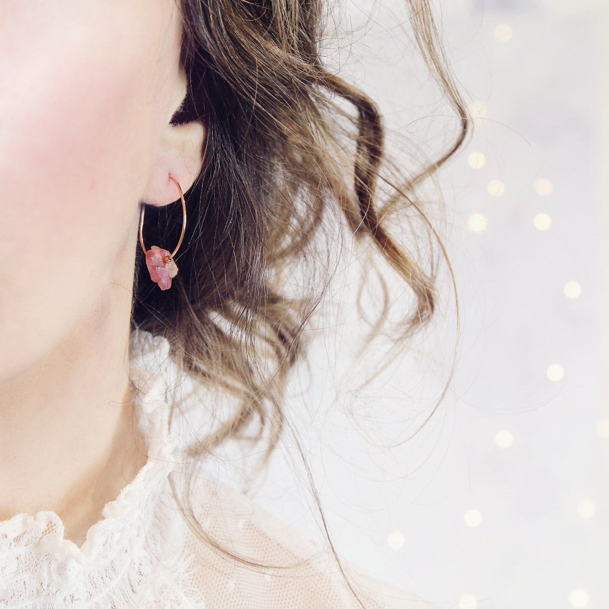 Close-up of a person wearing a pink tourmaline earring in rose gold metal with a soft focus background