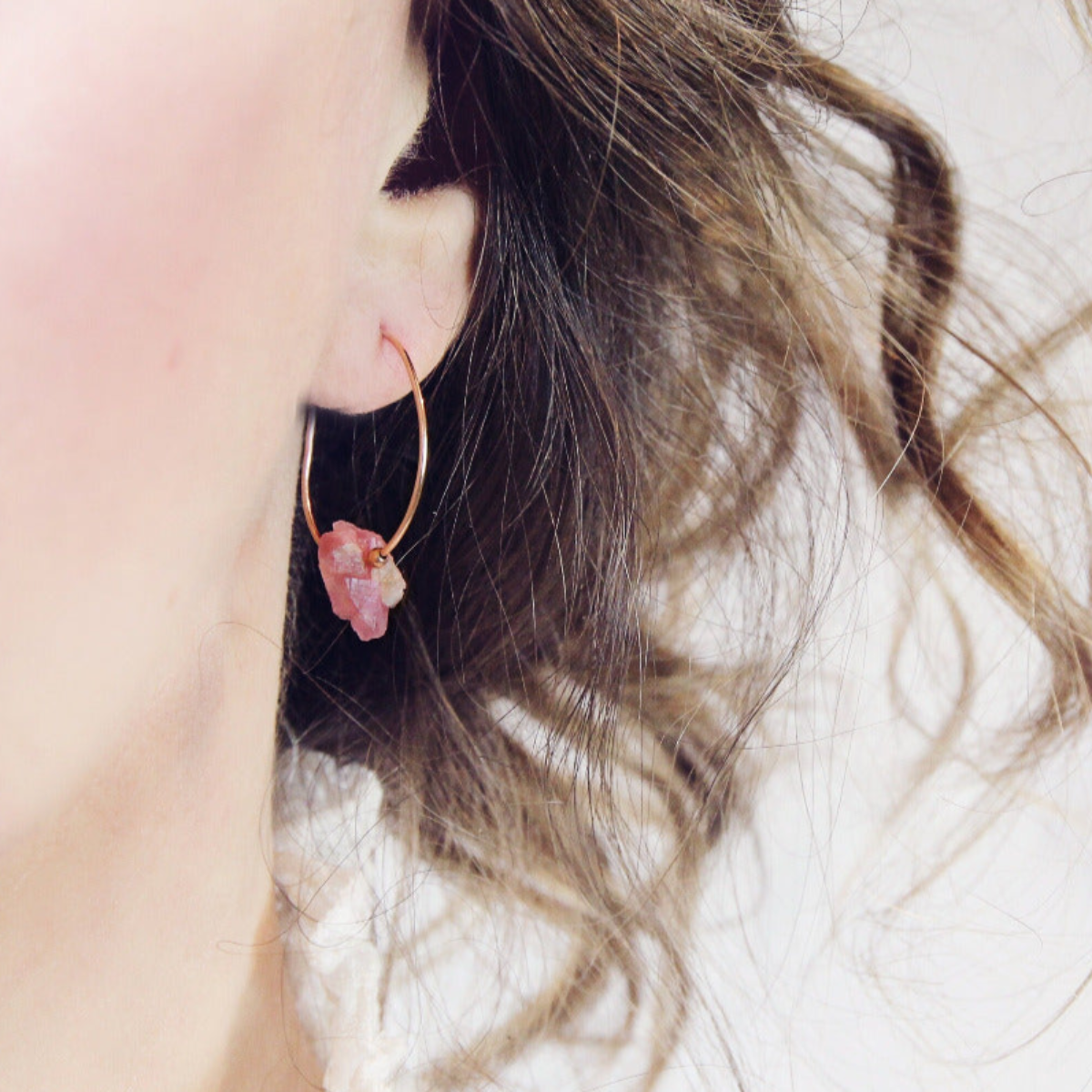 Close-up of a person wearing a pink stone earring with a blurred background