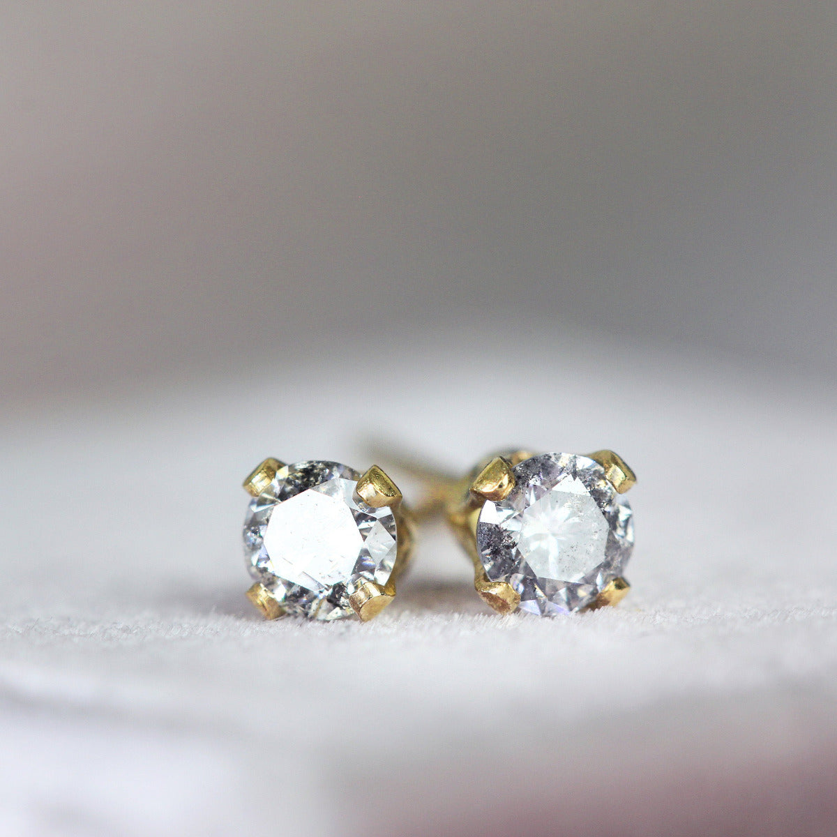 One pair of matching grey diamond stud earrings set in gold. The diamond is round, faceted and sparkling and grey flecked in colour. The stones are set into 14k gold fill ear posts with a 4 prong setting with matching butterfly backs.