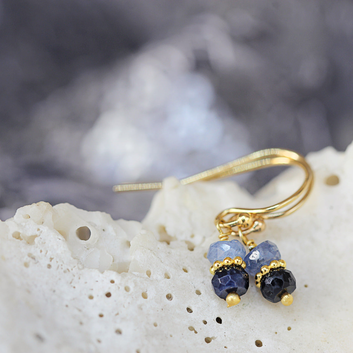 Gold drop earrings with blue sapphire gemstones on a textured surface