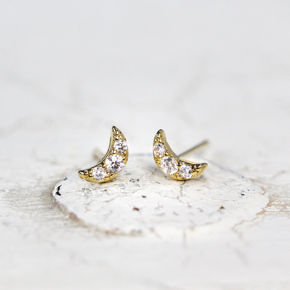 A pair of Tiny Crystal Moon Studs in Gold on a white background