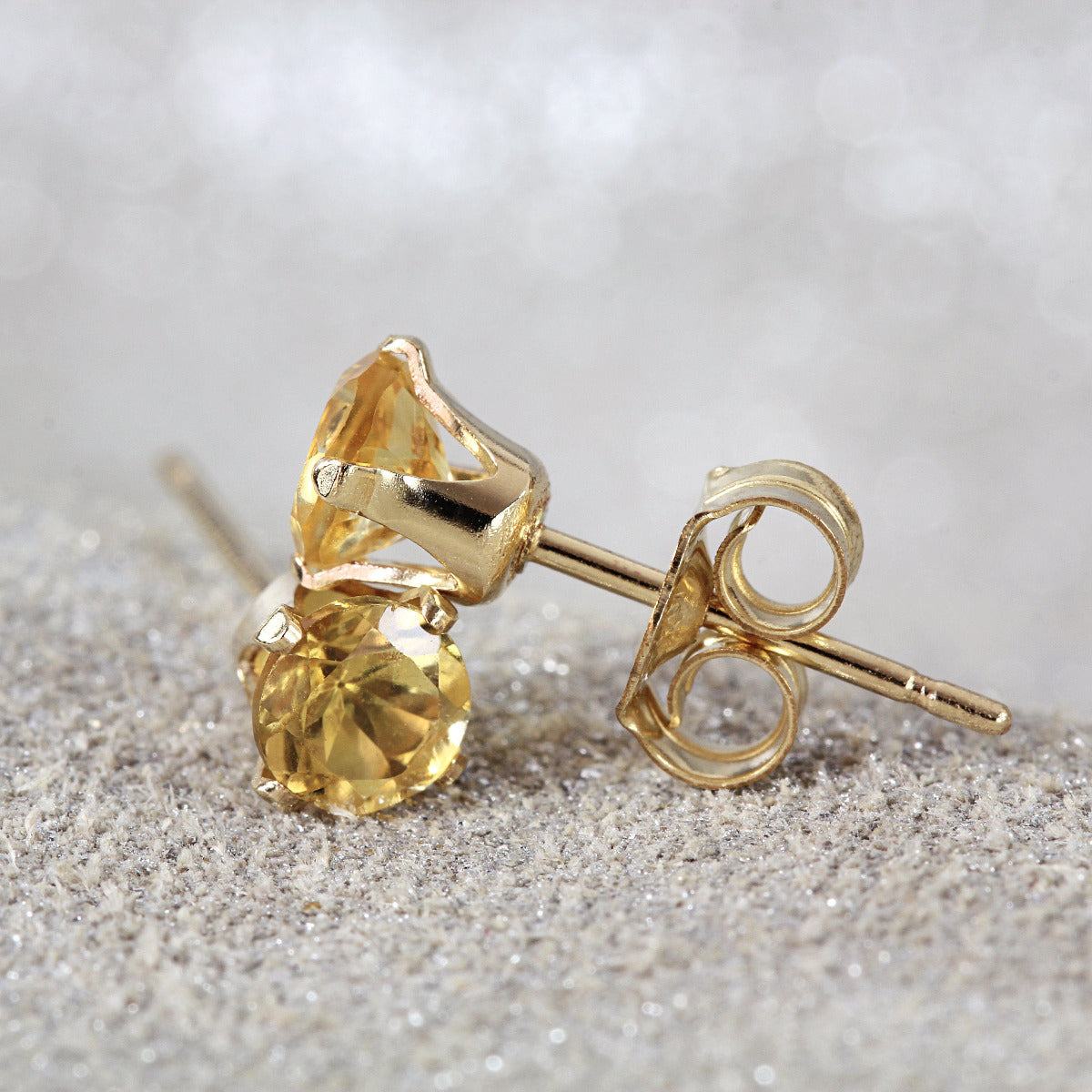 One pair of yellow citrine stud earrings. The stone is round in shape with a facted brilliant round cut. The 14k gold fill ear post setting has four prongs holding the gemstone in place, and butterfly push backs to secure the stud on the ear.