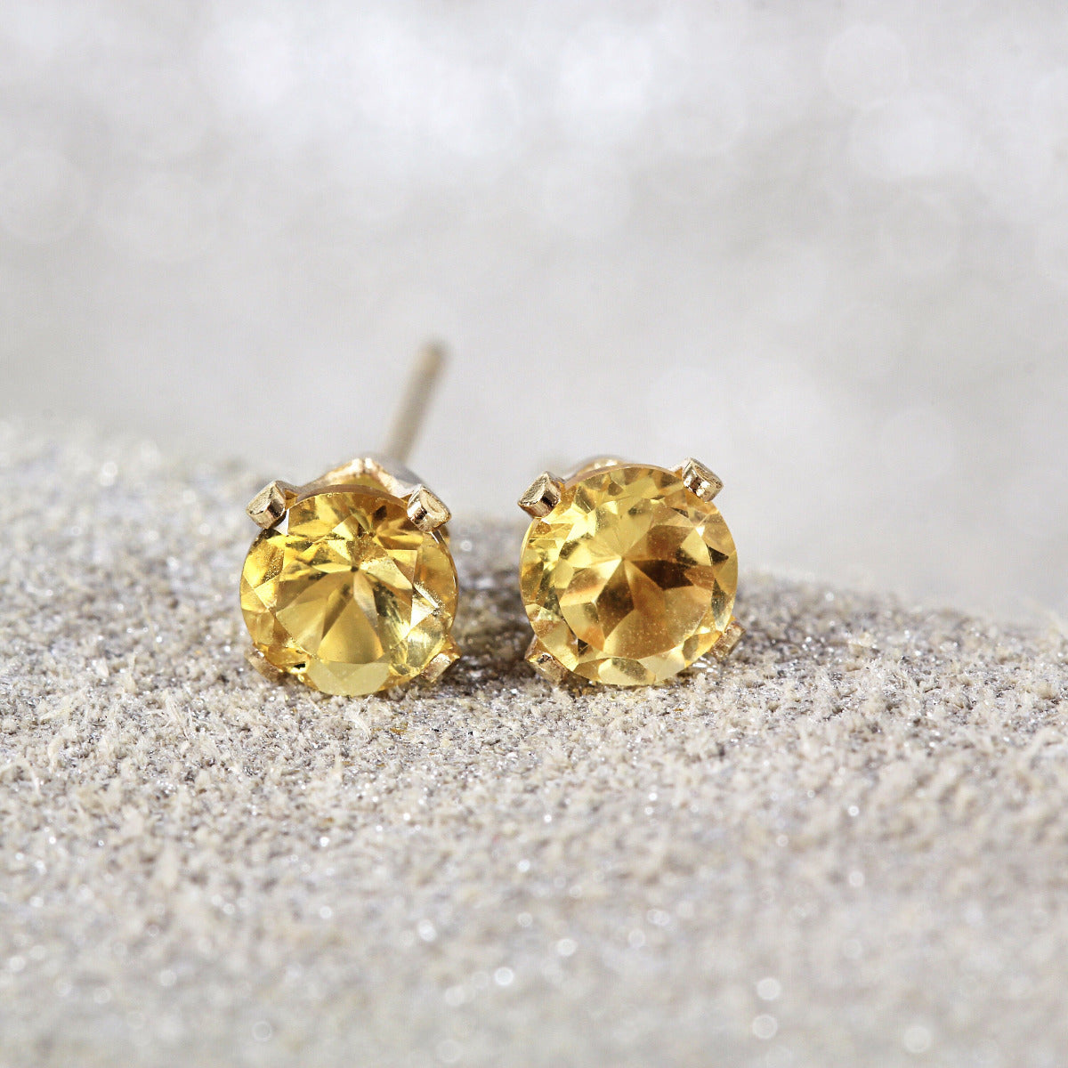 A pair of yellow citrine stud earrings. The citrine gemstones are sparkling and catch the light. The stones are a brilliant round cut with lots of facets, and set into gold filled four prong settings. Simple, minimal, round stud earrings.