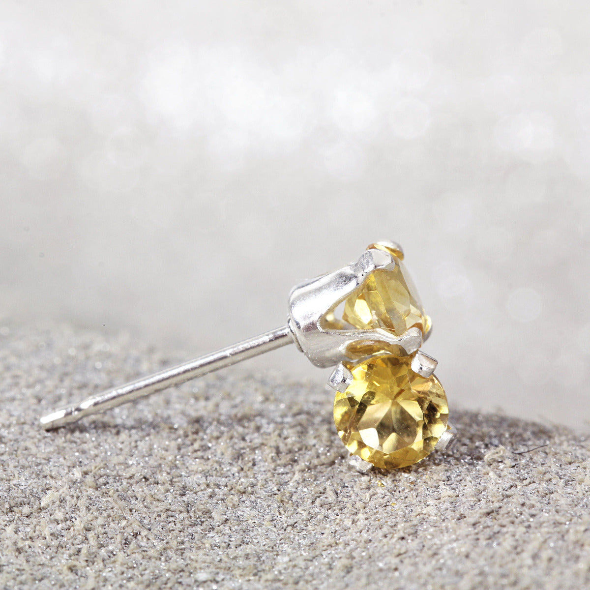 A pair of yellow citrine post earrings. The citrine gemstones are sparkling and catch the light. The stones are a brilliant round cut with lots of facets, and set into sterling silver prong settings. Simple, minimal, round stud earrings.