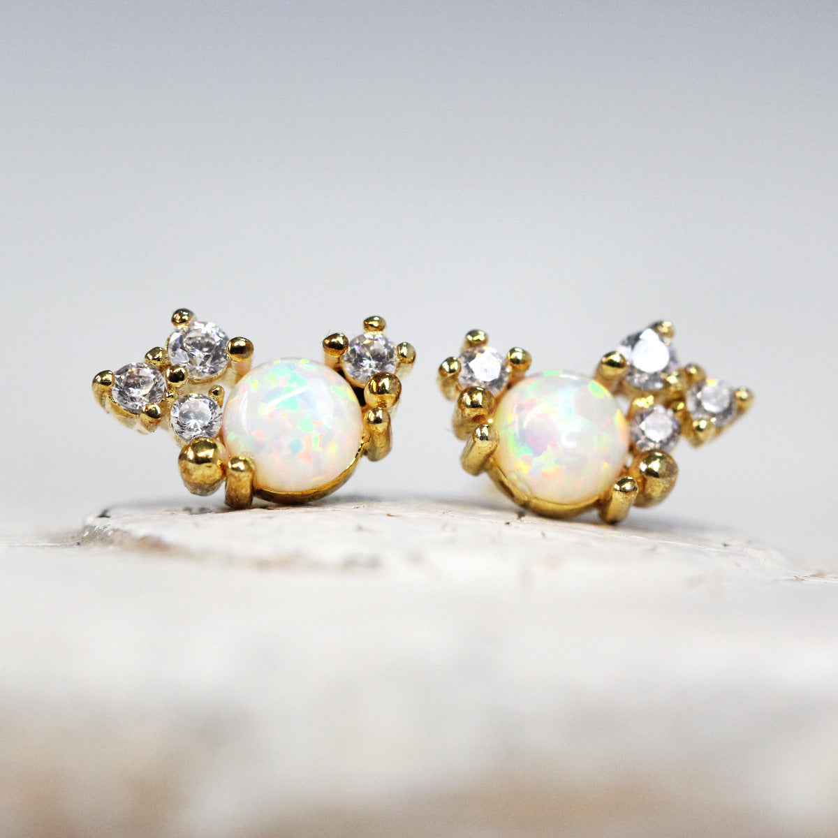 A pair of gold-colored stud earrings featuring a crystal cluster design with sparkling cubic zirconia and opal stones.