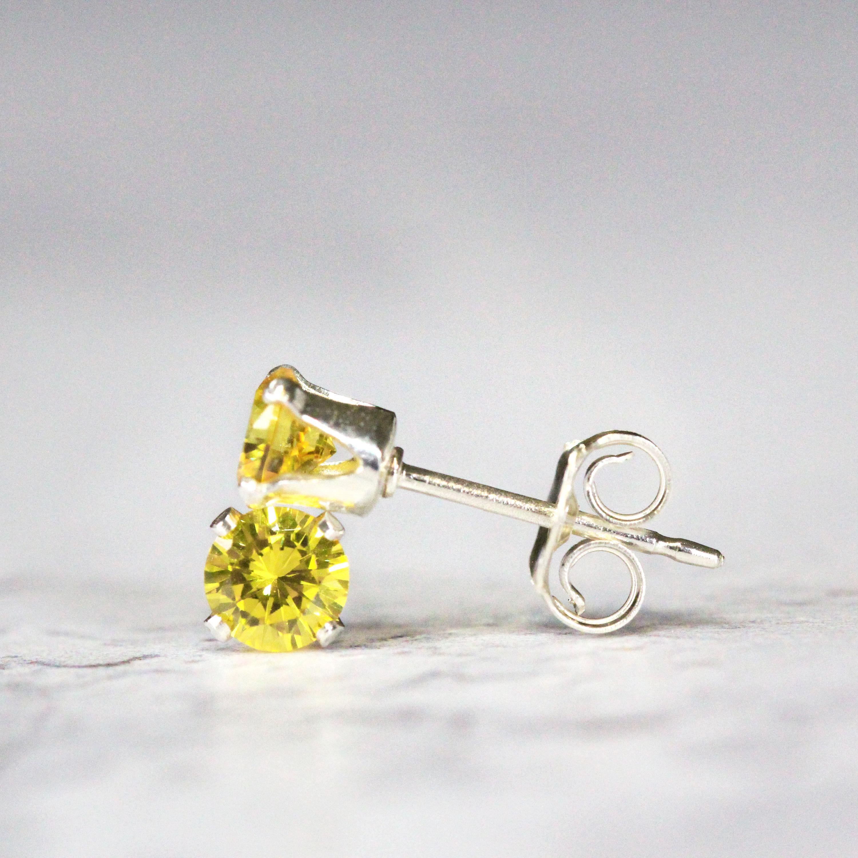 A pair of bright yellow cubic zirconia crystal gemstone stud earrings. The cz gemstones are sparkling and catch the light. The stones are a brilliant round cut with lots of facets, and set into sterling silver four prong settings. Simple, minimal, round stud earrings shown against a simple light background.