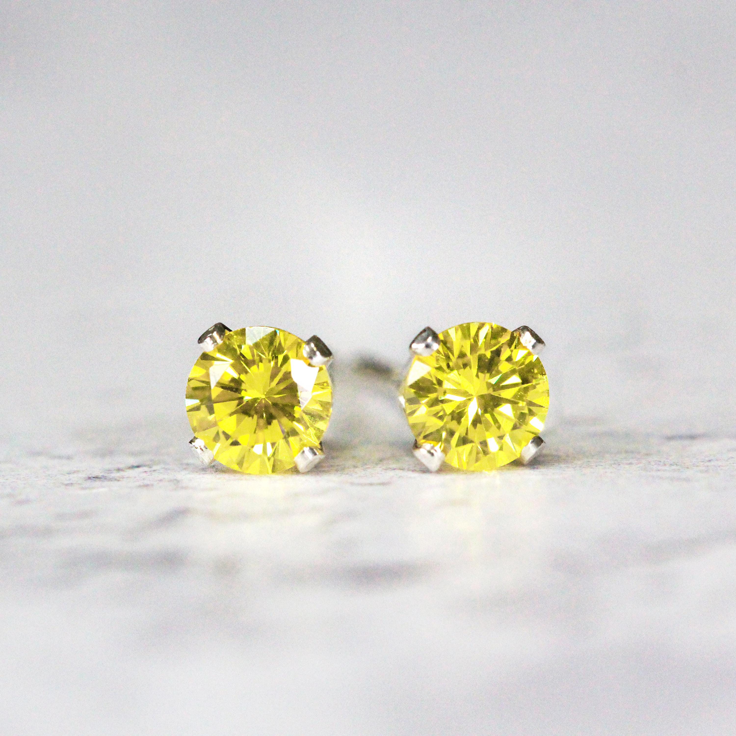 A pair of bright yellow cubic zirconia stud earrings. The cz stone is round in shape with a faceted cut. The sterling silver ear post setting has four prongs holding the gemstone in place, and butterfly push backs to hold the stud securely on the ear.