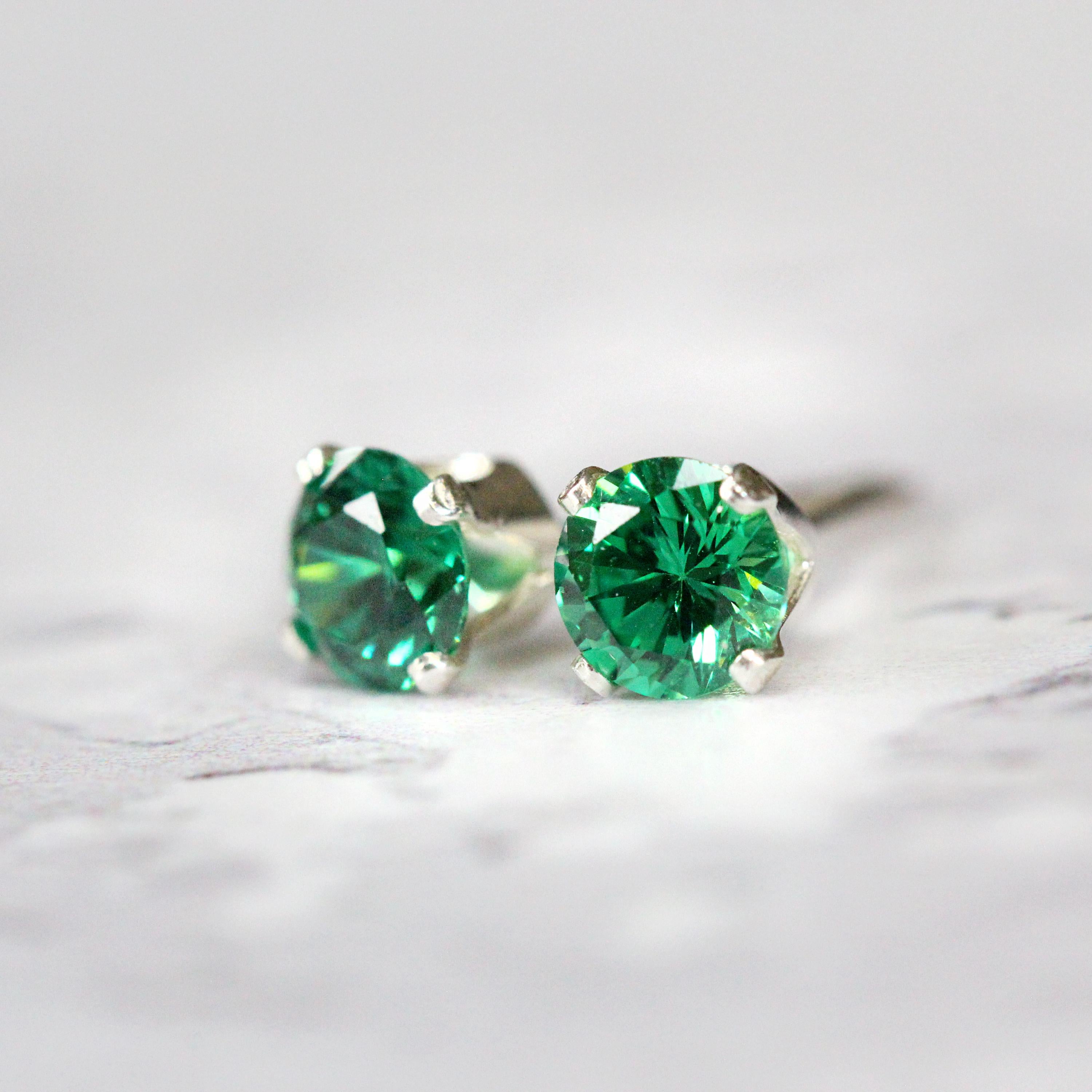 A pair of deep green cubic zirconia stud earrings. The cz gemstones are sparkling and catch the light. The stones are a brilliant round cut with lots of facets, and set into sterling silver four prong settings. Simple, minimal, round stud earrings.