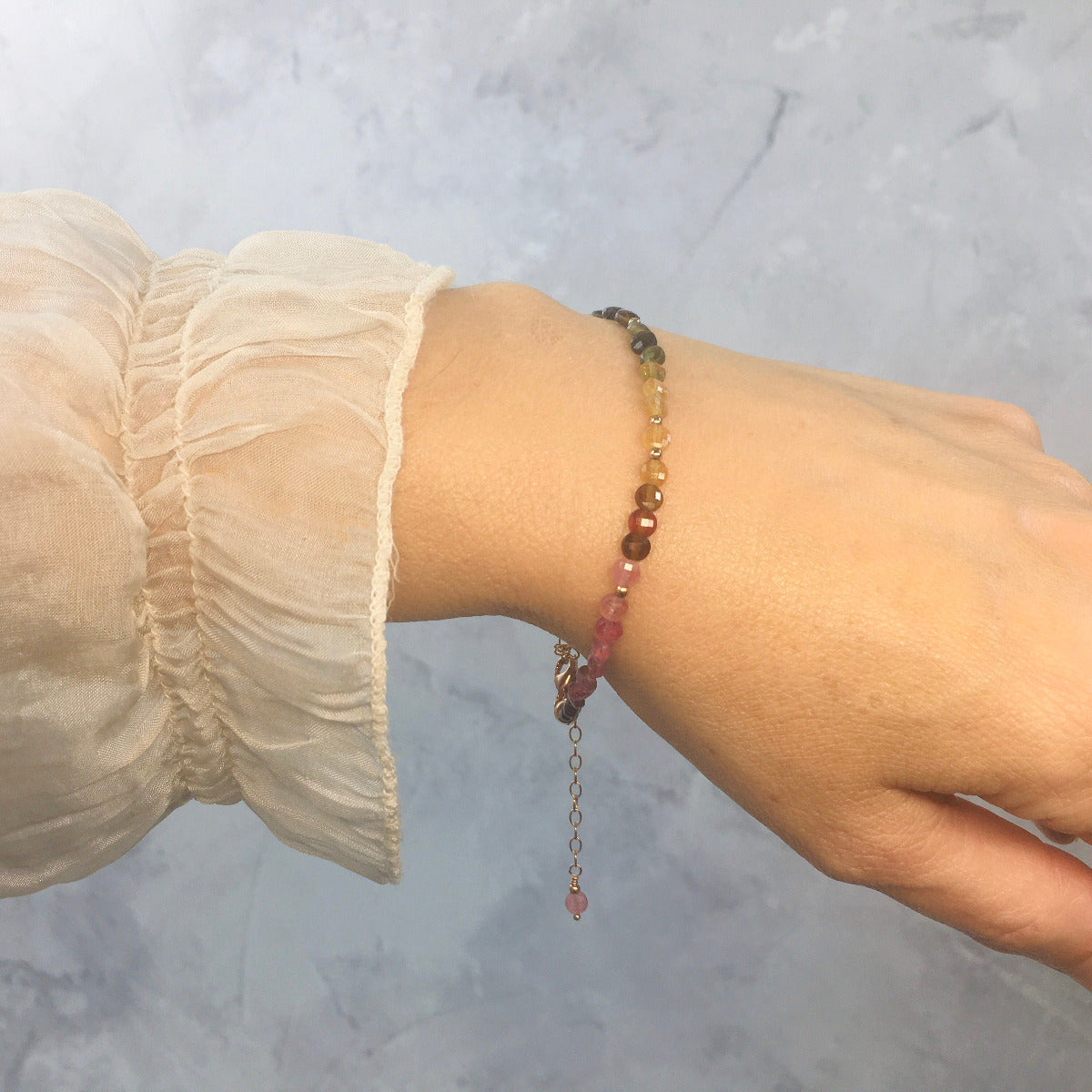Close-up of a wrist wearing a colourful tourmaline beaded bracelet against a light background