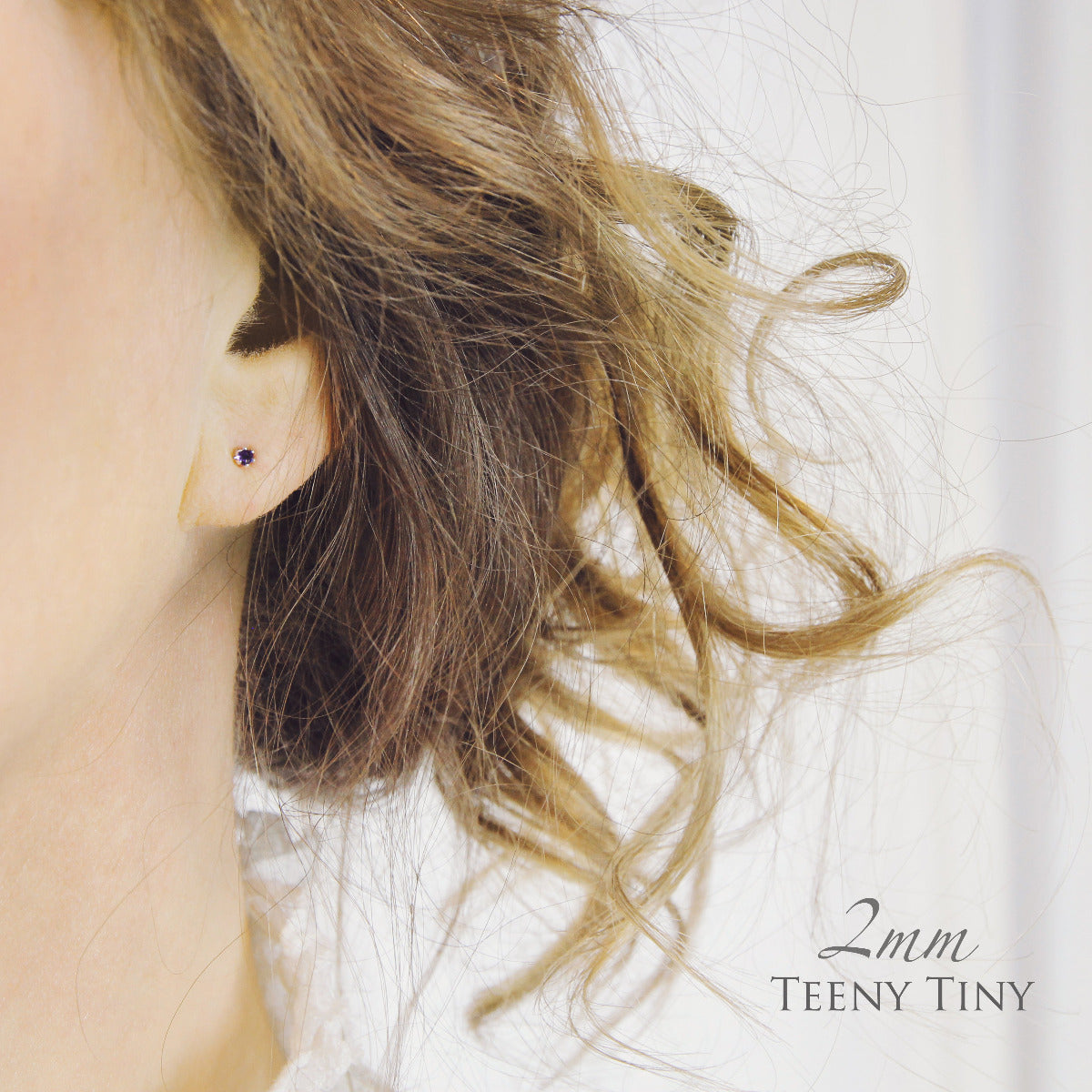 Close-up of an ear wearing a small 2mm stud earring, against a light background.