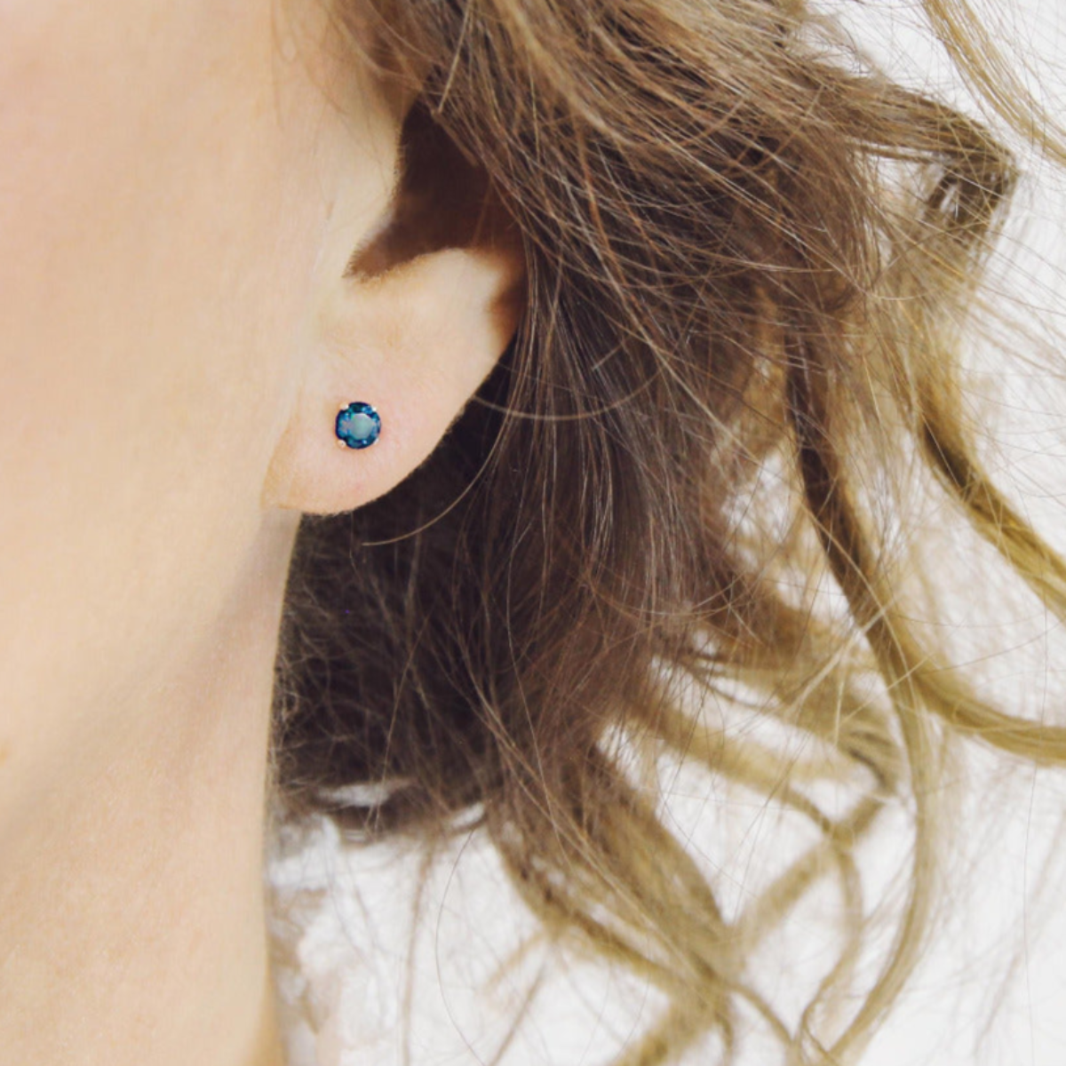 Close-up of an ear wearing a blue gemstone stud earring with blurred background