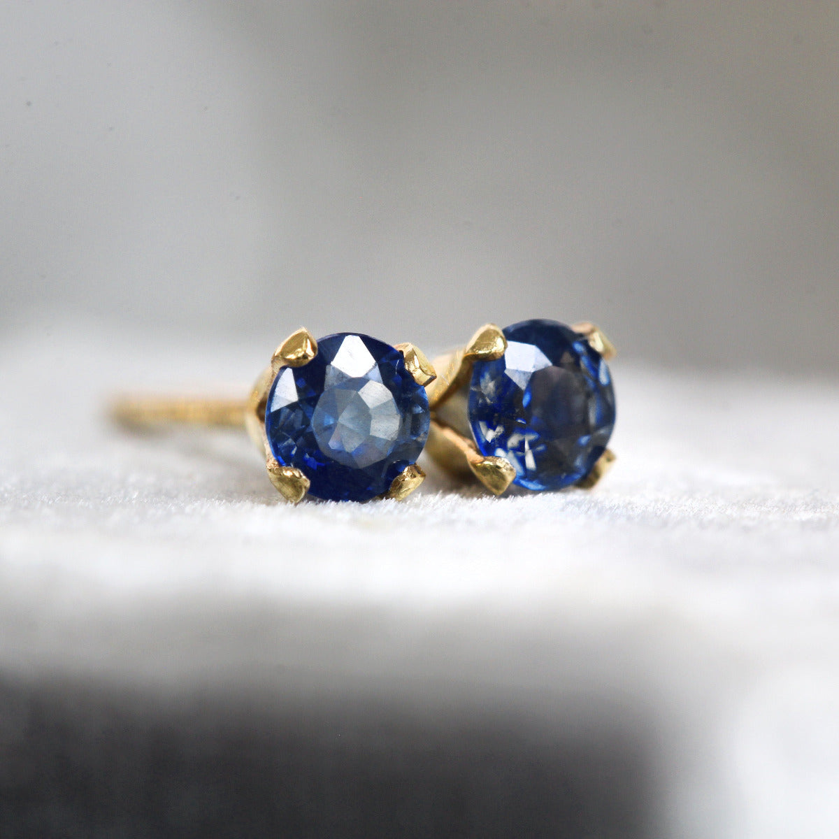Pair of blue sapphire gemstone earrings with gold settings on a white surface.