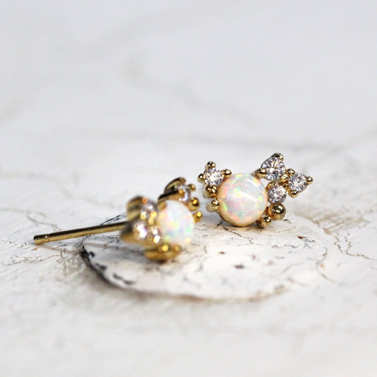 A pair of gold-colored stud earrings featuring a crystal cluster design with sparkling cubic zirconia and opal stones.