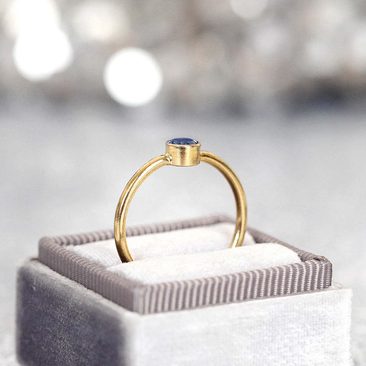 Gold ring with a blue gemstone on a gray jewelry box with a blurred background