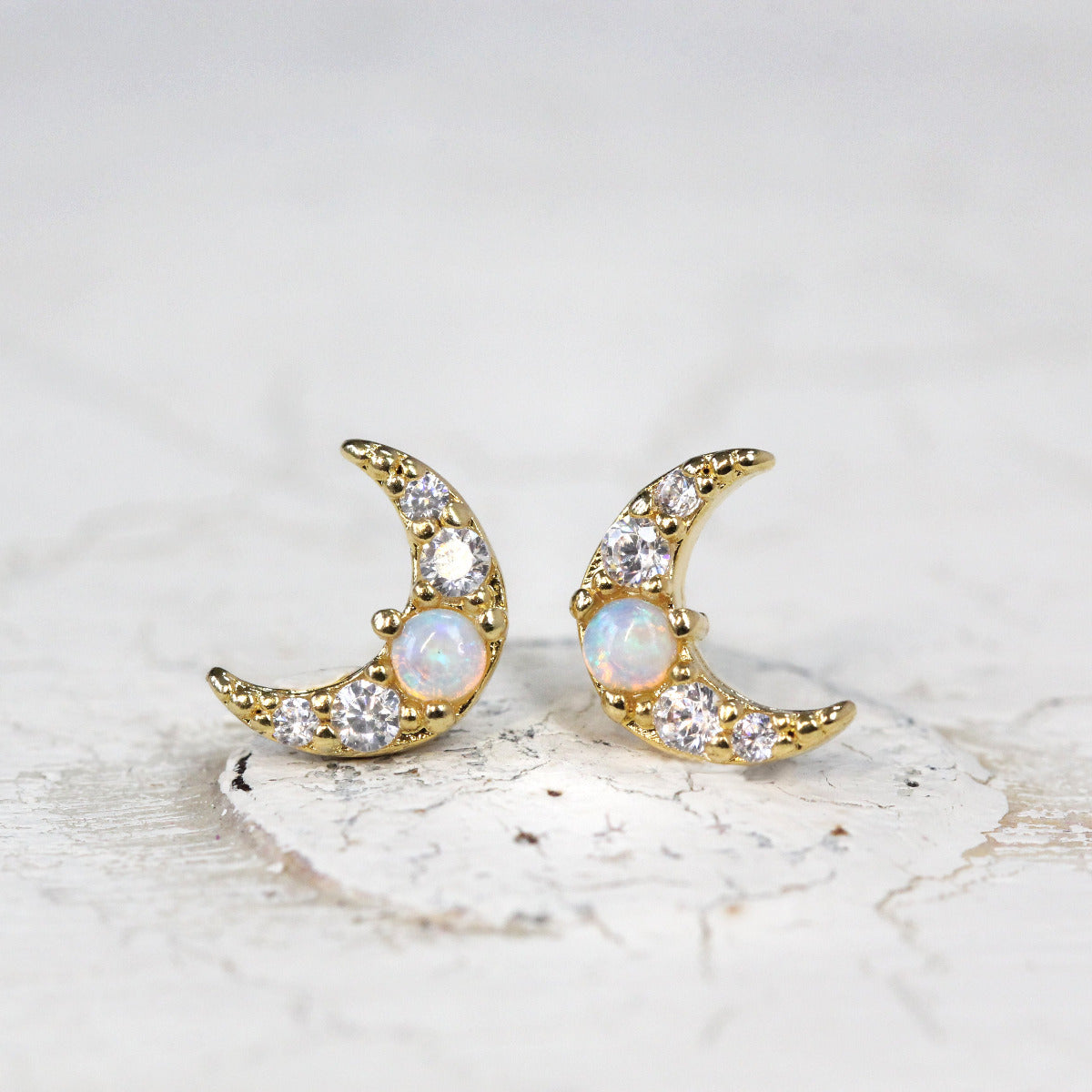 A pair of Crescent Moon Stud earrings with opal and crystal stones set in gold shown on a soft grey background