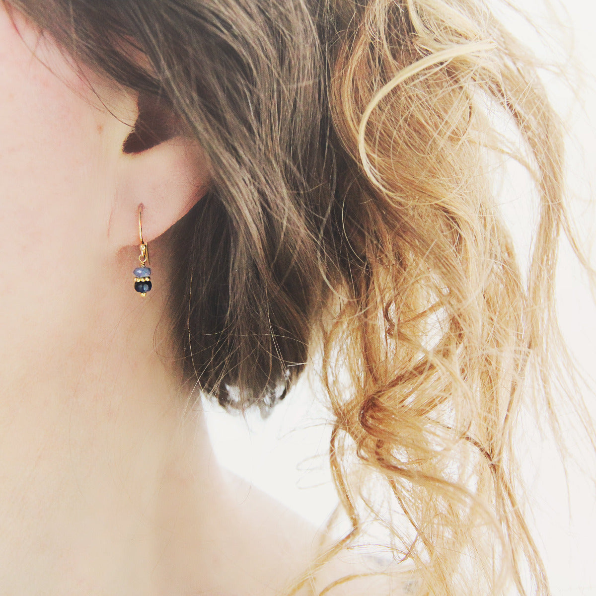Close-up of a blue sapphire drop earring worn by a person with wavy hair.