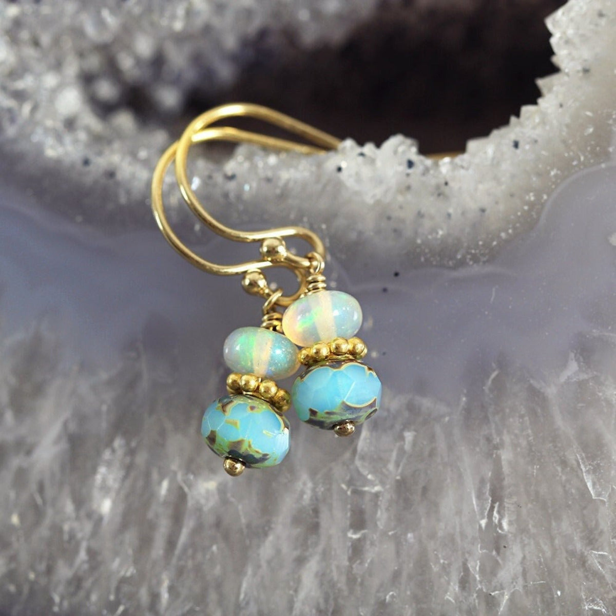 Handmade drop earrings featuring an iridescent opal gemstone bead hanging above a turquoise glass bead with a gold disc between. The beads hang from a small and dainty gold ear hook wire. The earrings are pretty, feminine and delicate in style.