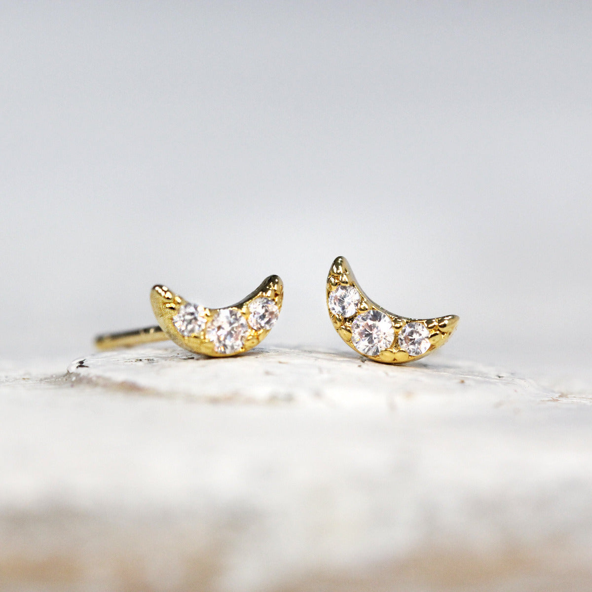 A pair of Gold stud earrings with crystal moon design on a soft white background