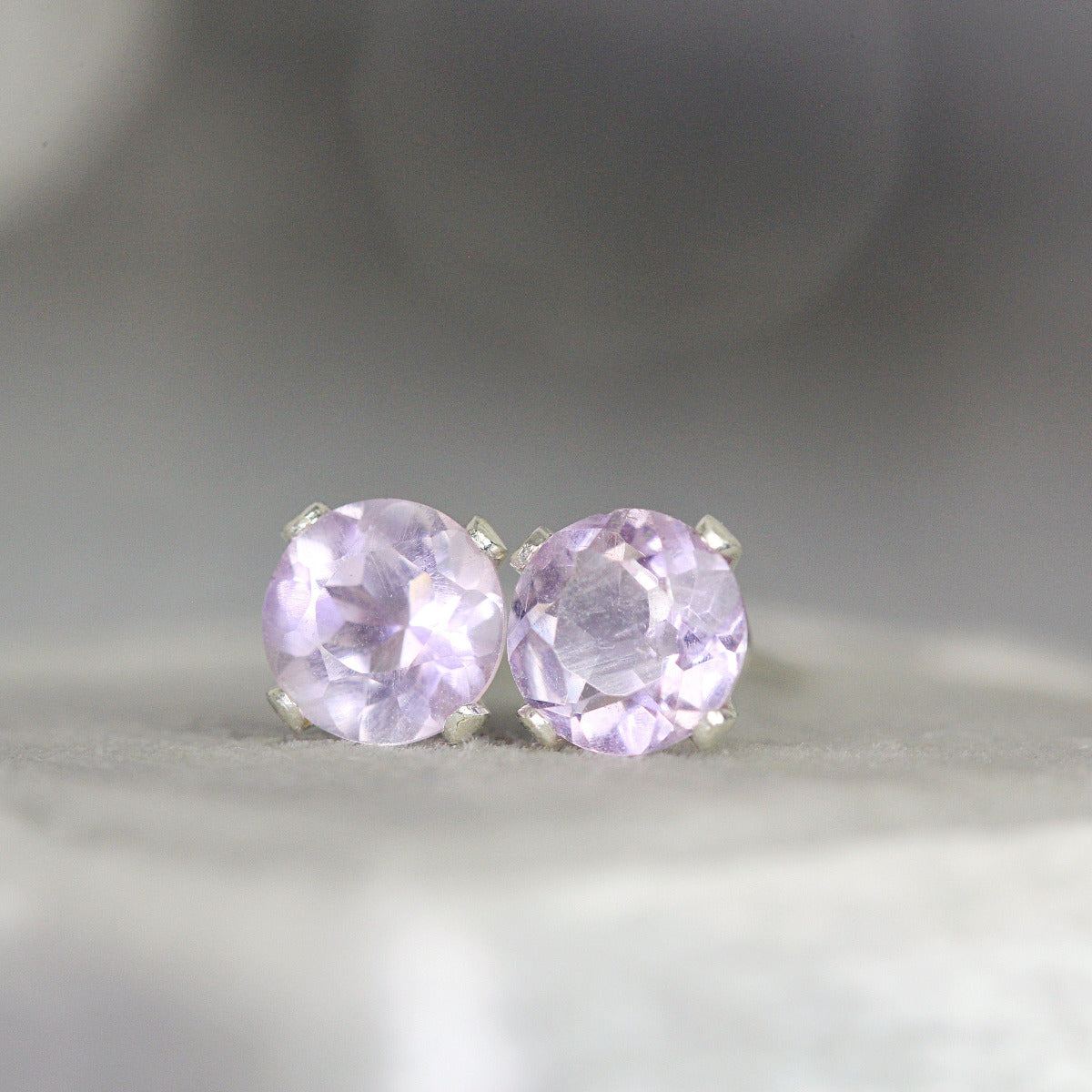 One pair of light purple amethyst stud earrings. The amethyst gemstones are sparkling and catch the light. The stones are a brilliant round cut with lots of facets, and set into sterling silver prong settings. Simple, minimal, round stud earrings.