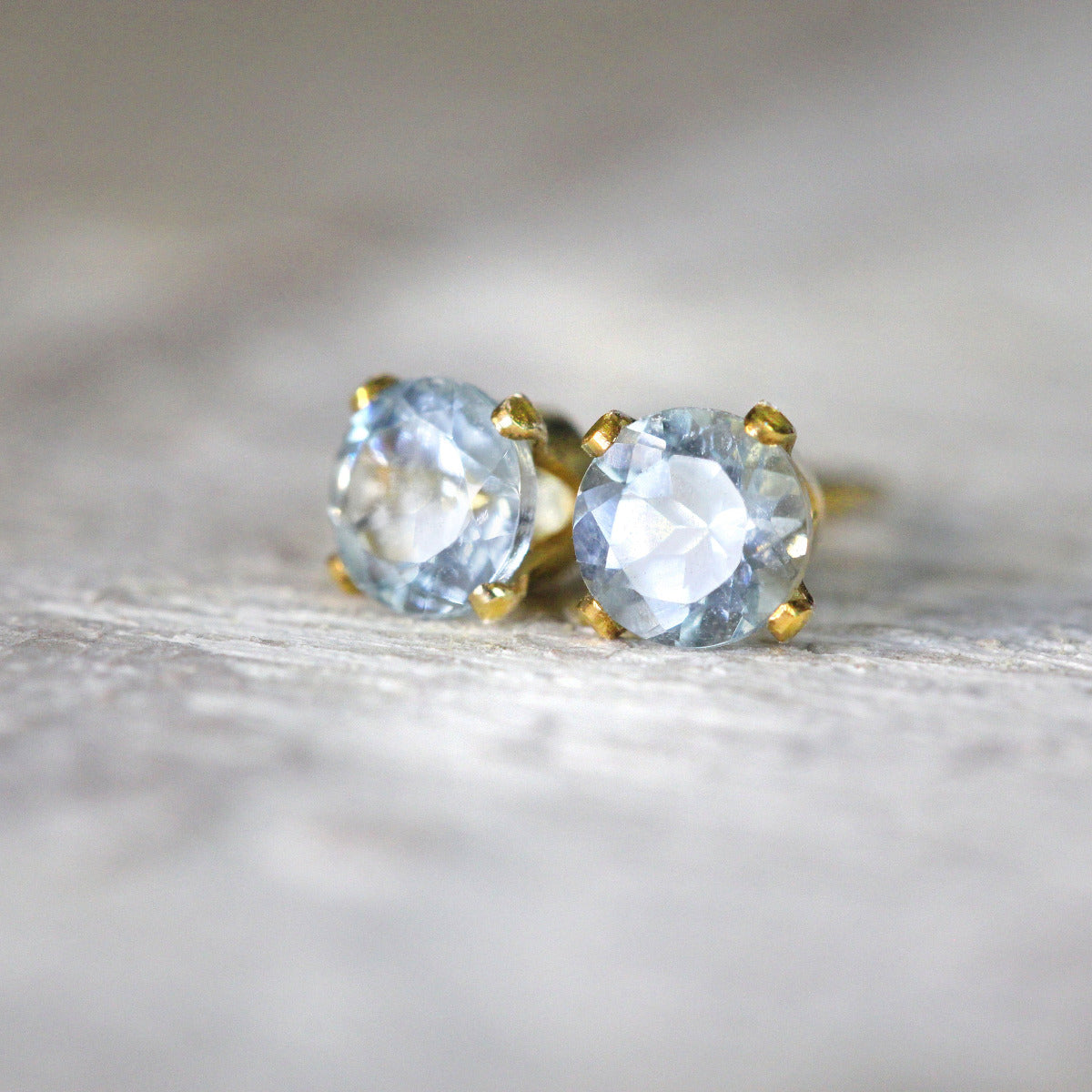 One pair of matching gemstone stud earrings in gold settings. The aquamarine gemstone is round, faceted, sparkling and pale blue in colour. The stones are set into 14k gold fill ear posts with a 4 prong setting with matching butterfly backs.