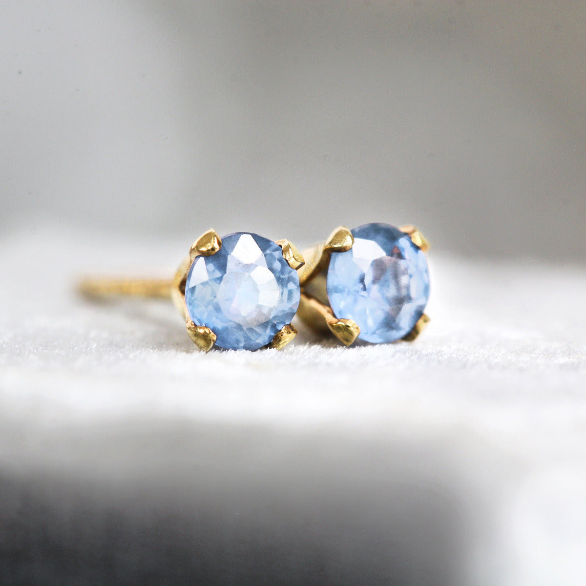 Gold earrings with blue sapphire gemstones on a light gray background