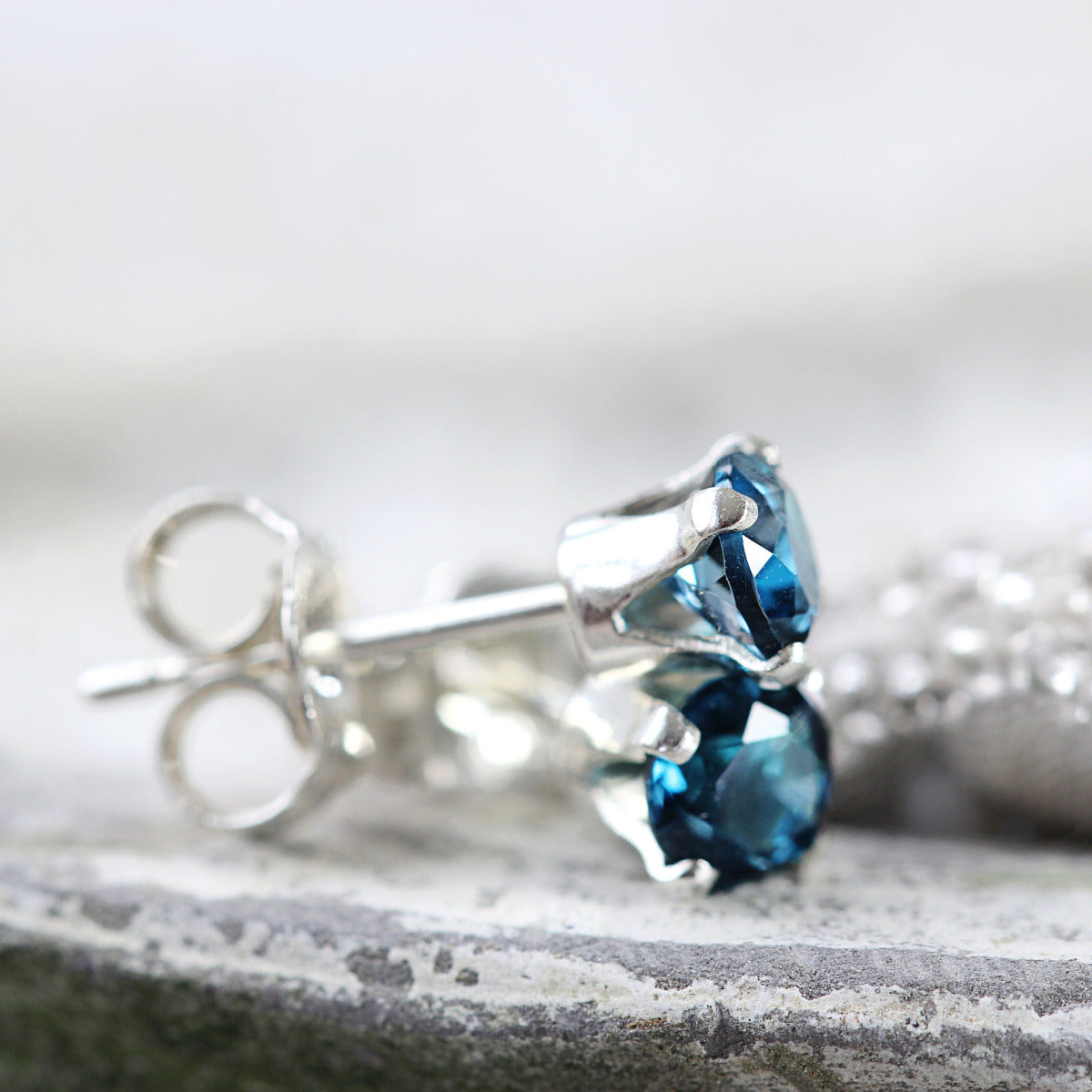 A pair of simple, minimal round stud earrings made with London Blue topaz gemstones set into sterling silver ear posts. Available in various sizes including 3 milimetres diameter, 4 milimetres diameter, 5 milimetres diameter and 6 milimetres diameter