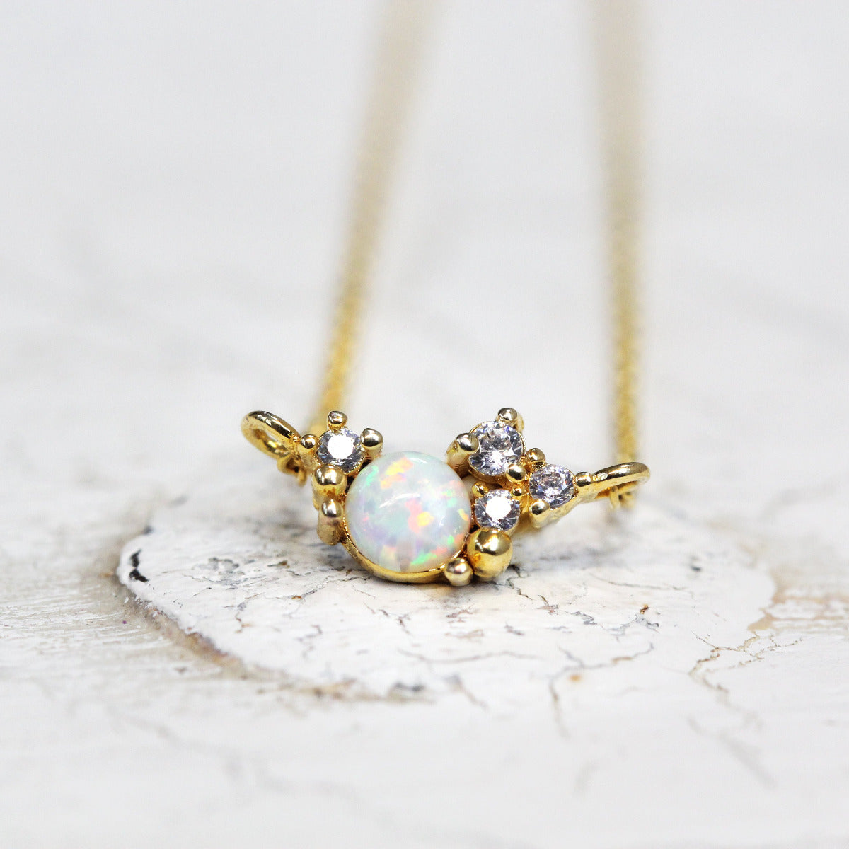 A gold-colored cubic zirconia birthstone cluster necklace with a gold-plated chain, displayed against a white textured background.