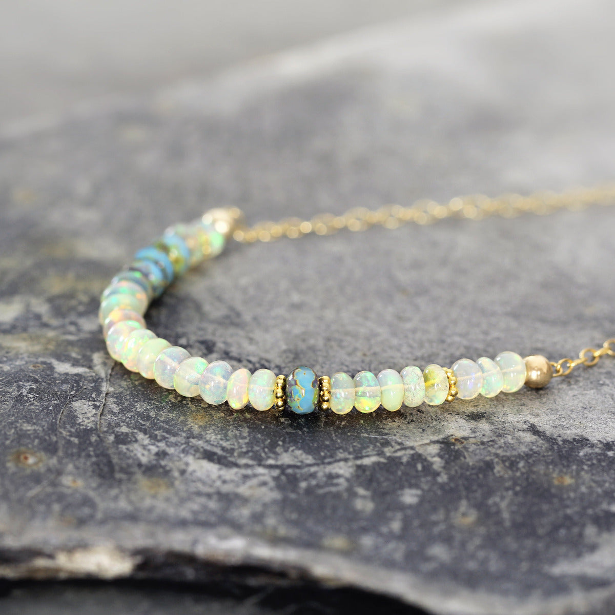 Delicate opal bead necklace with gold accents on a stone surface