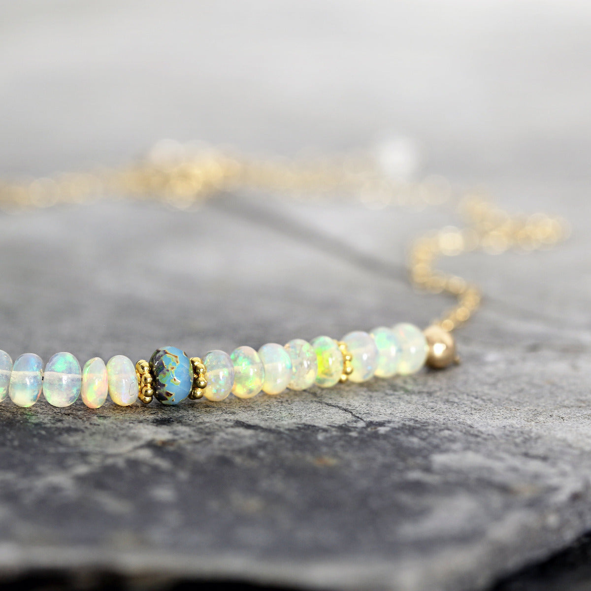 Opal beaded necklace on a gold chain with a gray stone background